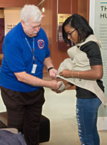 Docent assists student with putting on a pregnancy simulation vest